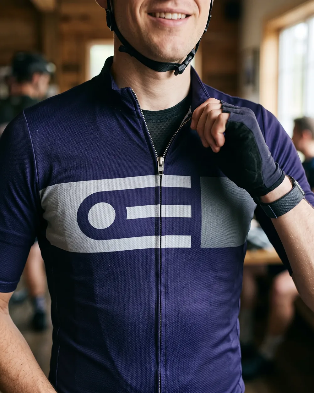 A rider pulling the front zip of a team jersey up to the collar, the chest panel lining up across both sides of the zip
