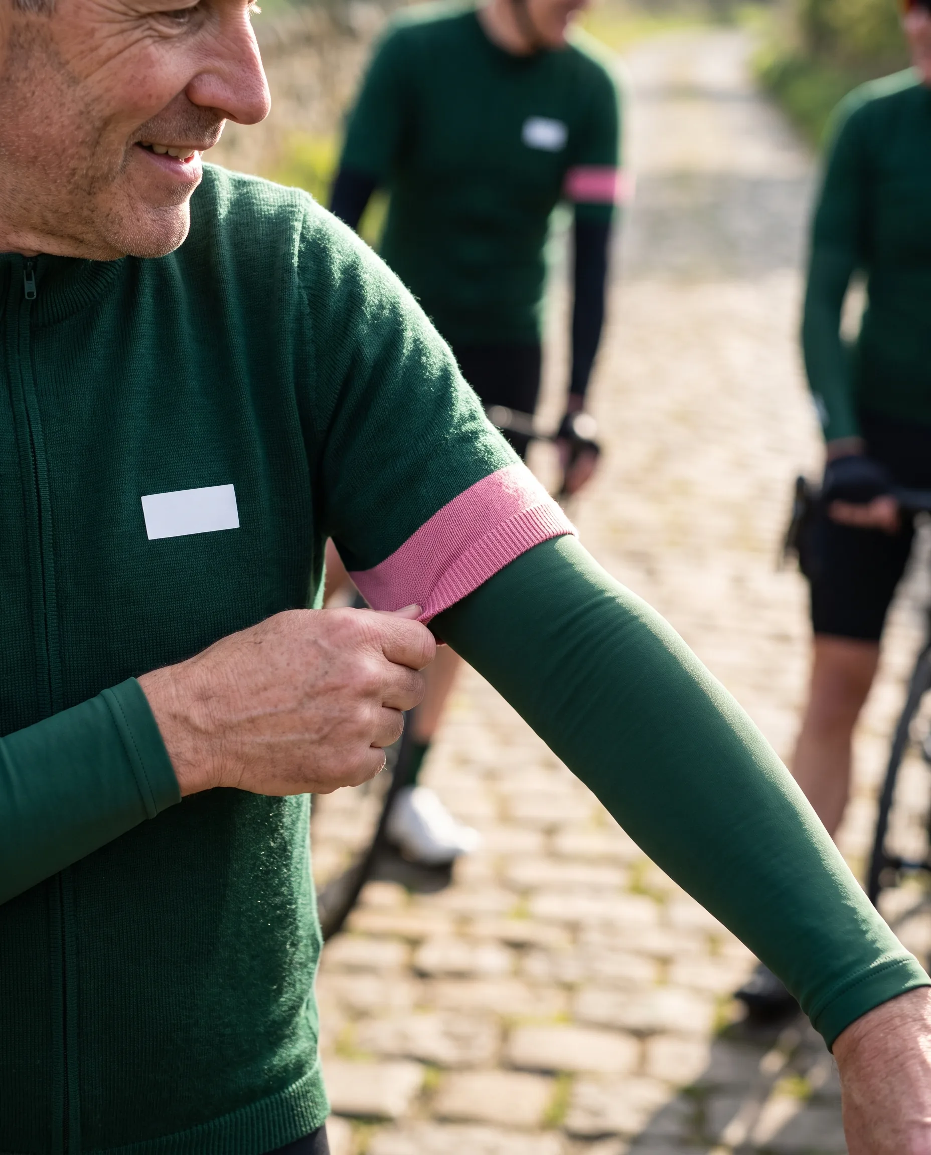 A club rider pulling up an arm warmer whose colour band meets the band on his jersey sleeve